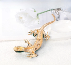 Vue détaillée de l'arrière d'une broche lézard dorée avec fermoir sur plateau blanc fleuri