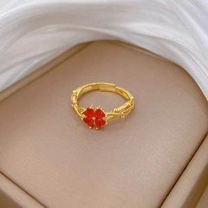 Bague trèfle dorée ajustable avec pierres rouges en cœur sur fond beige texturé