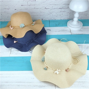 Vue détaillée de chapeaux de paille tissés avec bords ondulés et fleurs en tissu colorées