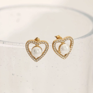 Elegant gold heart earrings with pearl and rhinestones displayed on a glass rim