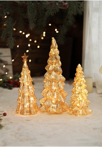 Detailed view of three sizes of glass Christmas trees with warm LED light in snow scene