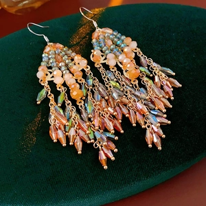 Close-up of bohemian tassel earrings with orange and amber beads on green velvet