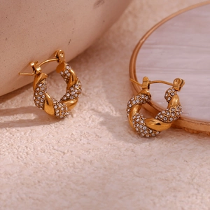 Detailed close-up of gold twist hoop earrings with pavé set zircon stones on stone tray