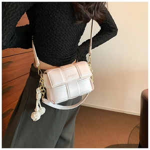 Détail du sac bandoulière blanc tressé avec chaîne dorée et décoration de nœud