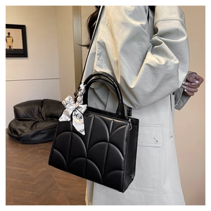 Detail of black quilted handbag with silk scarf handle on a trench coat model
