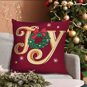 Dark red Christmas JOY pillow cover with wreath on a grey sofa near festive tree