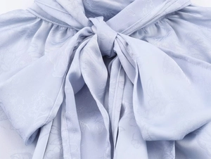 Detail einer hellblauen Jacquard-Satinbluse mit stilvollem Schleifen-Ausschnitt-Design
