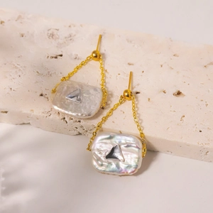 Baroque freshwater pearl earrings with gold chain and triangle crystal on stone background