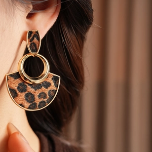Close-up of leopard print fan-shaped earrings with gold metallic frames on a model