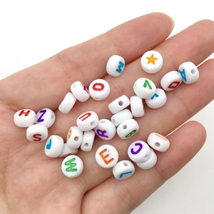 Close-up of white round acrylic beads with colorful letters held in a hand for DIY crafts