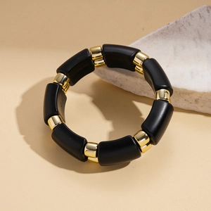 Close-up of matte black rectangular beads and polished gold spacers on an elastic bracelet