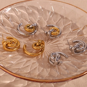 Detail of twisted knot gold and silver C-shaped earrings in a textured glass dish