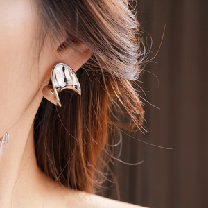 Close-up of minimalist silver C-shaped metal stud earring worn on model's ear