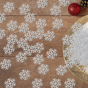 Sparkling silver snowflake confetti scattered on a wooden table with festive decor