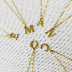 Gold plated stainless steel initial necklaces with letters E M A N O C on white fabric