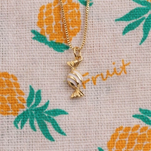 Detail view of a gold-plated lollipop pendant necklace with white enamel on fabric