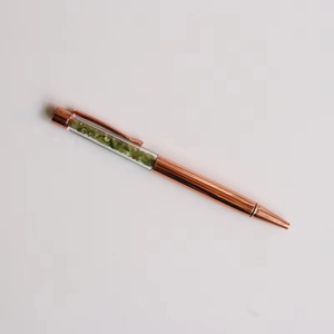 Detail of rose gold ballpoint pen featuring green crystal stones in a clear barrel