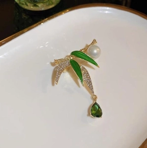 Detail view of a gold bamboo brooch with green enamel, sparkling crystals, and pearl