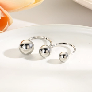 Detail of minimalist silver-plated U-shaped rings with spherical ends on ceramic plate