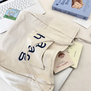 Flat lay of cream canvas tote bag with navy haag print and everyday lifestyle essentials