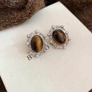 Macro view of oval tiger eye stud earrings with white pearl trim on brown knit fabric