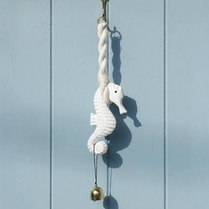 Minimalist wooden seahorse wind chime with brass bell on light blue background