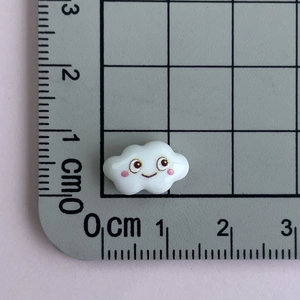 Mini resin cloud accessory with smile face on a measurement grid for size reference