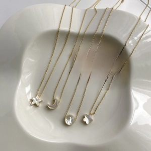 Detail of gold star and moon necklaces with natural mother of pearl charms on a ceramic tray