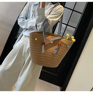 Detail of woven khaki tote bag featuring colorful pom-pom charms and striped strap