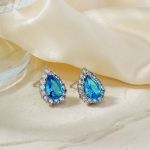 Teardrop blue zircon earrings with halo stones on elegant satin and stone background