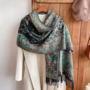 Detail of ethnic paisley tassel shawl styled with an off-white coat on wooden hanger