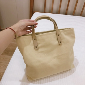 Detail of beige canvas tote bag featuring brown leather handles with metal rivets