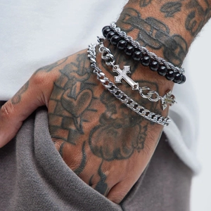 Close-up of men's layered cross pendant chain and black beaded bracelet on tattooed arm