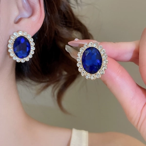 Detailed close-up of oval sapphire crystal earrings with classic white diamond halo