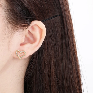 Close-up of golden heart-shaped stud earring with paved crystals on a model's ear