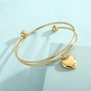 Detail of a golden double-wire bracelet featuring a smooth heart pendant on light blue background