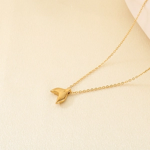 Detailed view of golden fish tail pendant necklace with hammered texture on beige background