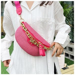 Detail of pink straw fanny pack with gold chain and horse charm worn in outdoor setting
