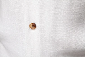 Macro shot of white linen shirt fabric featuring a natural amber-colored button detail