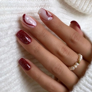 Deep red glitter blush press-on nails with heart patterns on warm sweater background