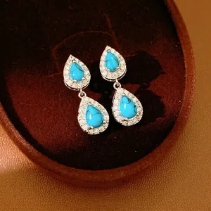 Vintage pear-cut turquoise earrings with sparkling halo set in silver on dark velvet