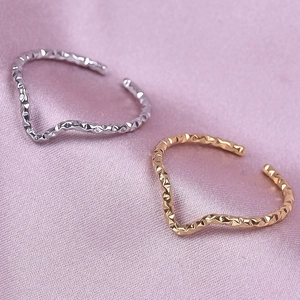 Detail of gold and silver wave V-shaped rings with hammered finish on pink silk