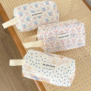 Dreamy quilted floral makeup bags with carry handles displayed on a wicker chair