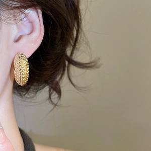 Detail of a golden textured twisted earring with vintage quilted relief pattern on model