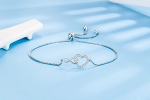 Detail of adjustable silver bracelet with heart and infinity symbol set with zircons