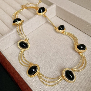 Close-up of golden multi-strand necklace with oval black gemstones in a beige jewelry box