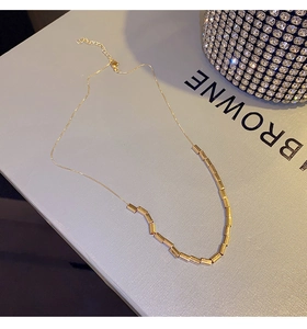 Detail of minimalist gold tube necklace with O-chain and lobster clasp on light grey stand