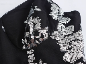 Nahaufnahme eleganter silberner Pailletten-Blumenmuster auf schwarzem Netz-Abendkleid