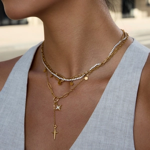 Détail de colliers superposés dorés avec pendentifs étoile, croix et diamants