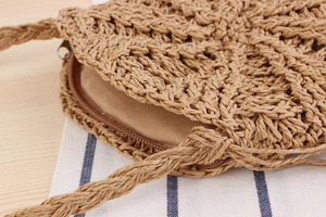 Detail of round straw bag showing the metal zipper closure and woven paper rope texture